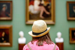 Girl in a hat looks at paintings in a museum