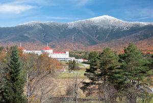 Colorful autumn scene at Bretton Woods, New Hampshire. Blue sky with dusting of snow on summit of Mount Washington, vibrant fall foliage, and red roof of historic Mount Washington Hotel.