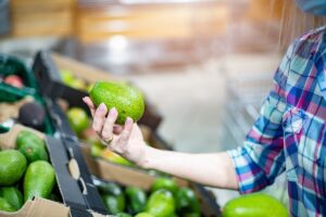 Woman customer choosing avocados in the supermarket. Close up of woman hand holding avocado.