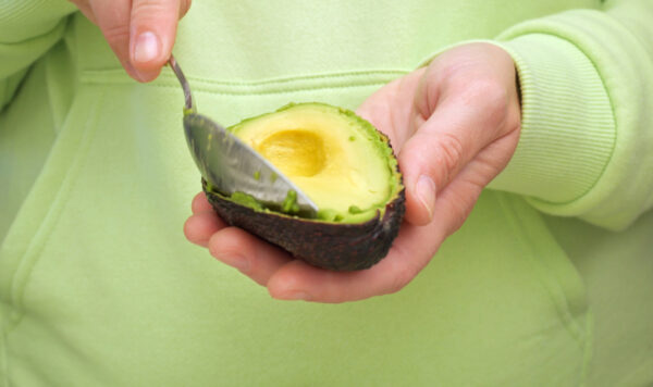 Woman shows sliced avocado. Close-up of a woman scooping out an avocado pulp with a spoon. Vegetarian food concept. Foods with vitamin E, avocado oil and antioxidants. Conscious nutrition concept.