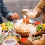 Cropped view of senior man holding bun while sitting near son at table with thanksgiving dinner.