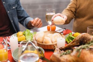 Cropped view of senior man holding bun while sitting near son at table with thanksgiving dinner.